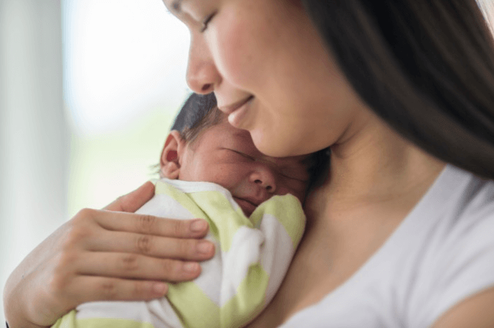 A photo of a woman holding a newborn baby against her chest.