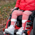 A photo of a child wearing a red jacket in a wheelchair on a trail wearing ankle foot orthoses.